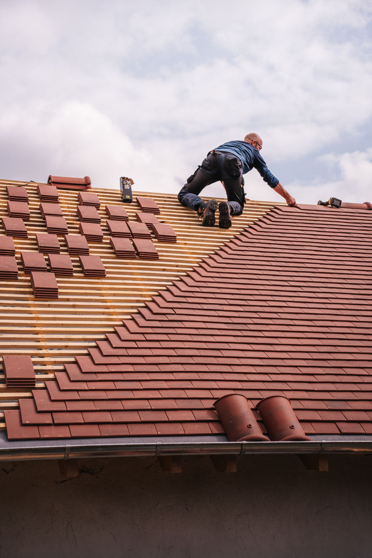 Roofer setting shingles on a new roof under a cloudy sky